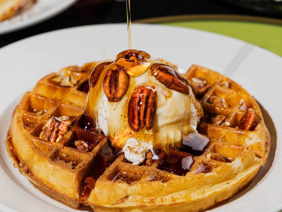 A waffle topped with ice cream, pecans and a stream of syrup