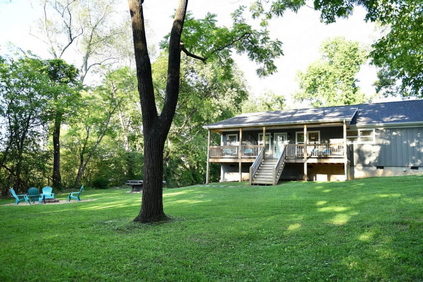 The grey board-and-batten house seen across a wide lawn with mature trees